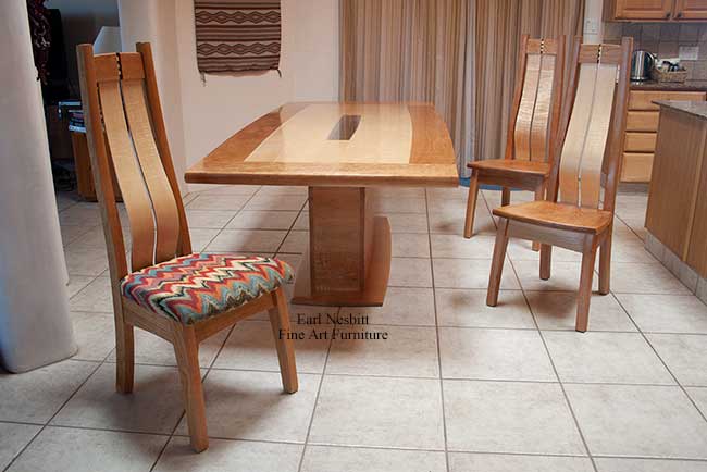 custom made contemporary dining table shown with three of four chairs, chair with upholstered seat is in foreground